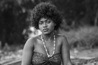 Black and white portrait of a woman with a natural hairstyle and traditional African necklace outdoors.